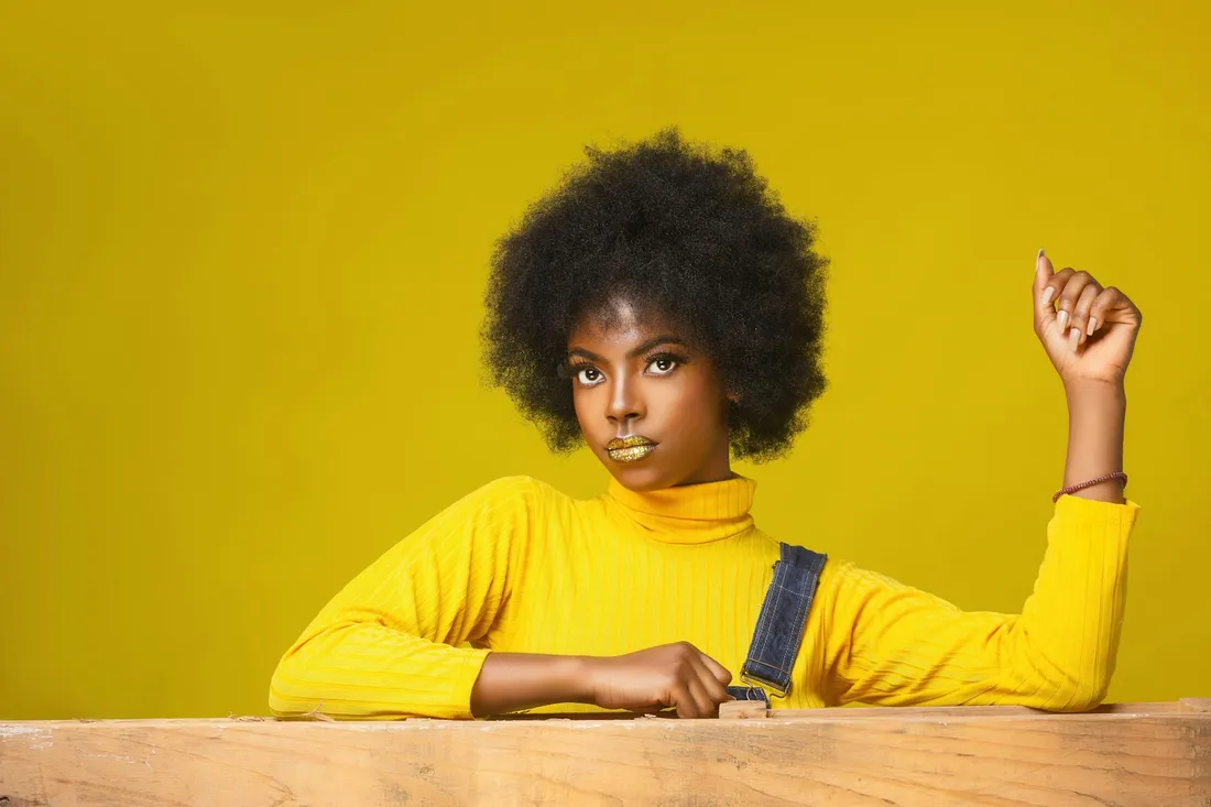 A young woman in a yellow sweater smiling against a bright yellow background