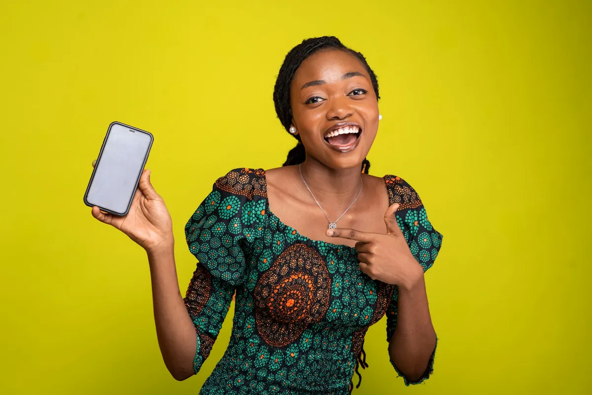 A smiling young woman holding up her phone to show the screen