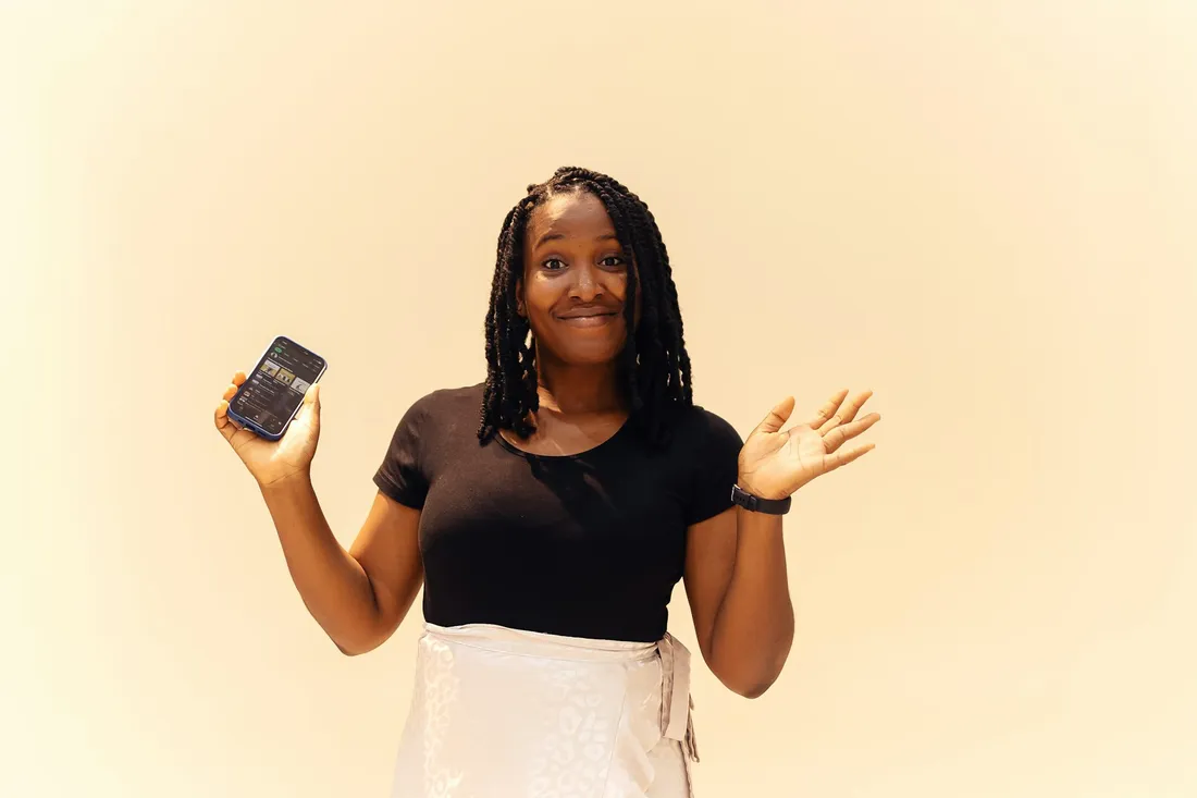 A smiling woman holding up her phone against a warm cream background