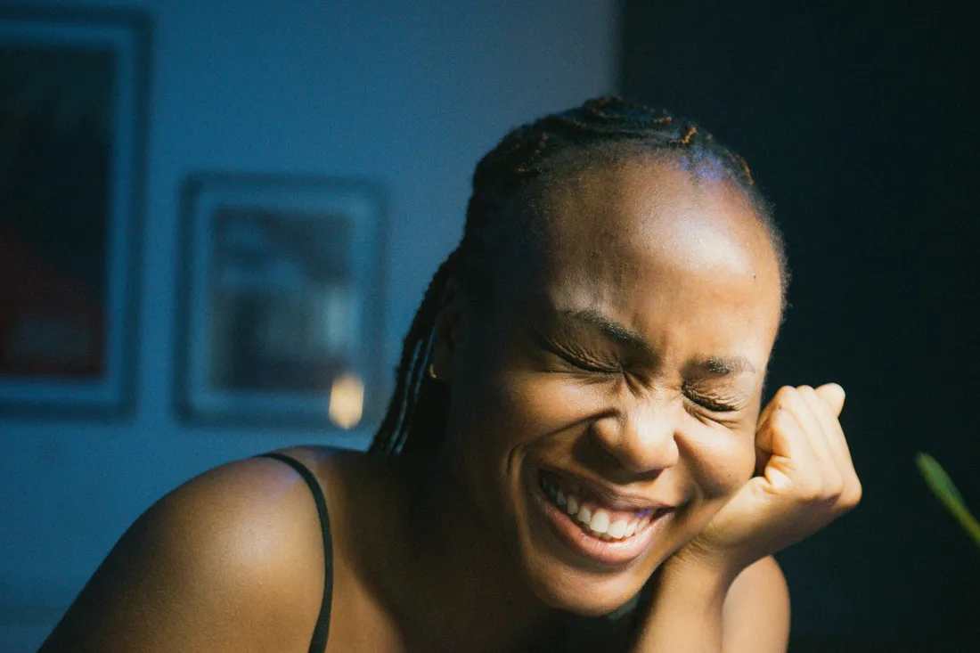 A woman laughing with her eyes closed, lit by warm light against a blue background