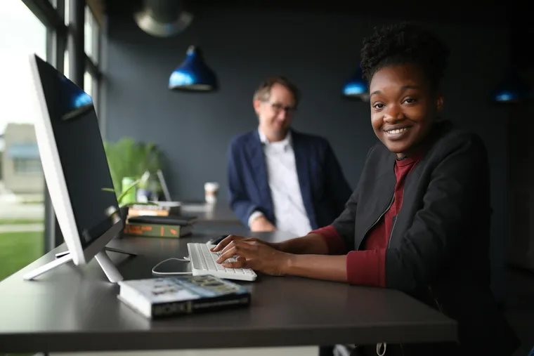 A smiling professional at a desktop computer in a modern office