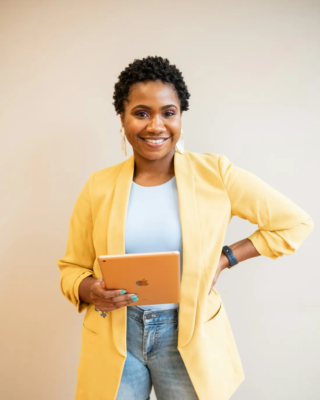 A smiling woman in a yellow blazer holding a tablet